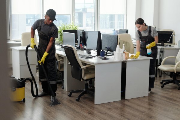 Young man and woman using detergent and vacuum cleaner for cleaning openspace office urban fresh